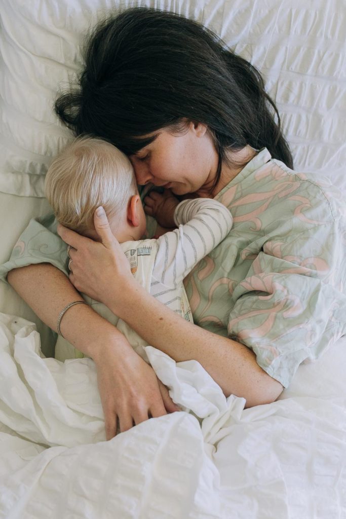 Mother laying in bed while cuddling with her 18 month old baby.